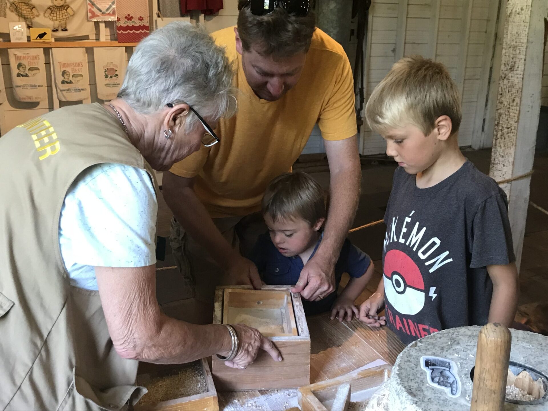 A museum volunteer shows children how to separate the parts of a grain from the fine flour.