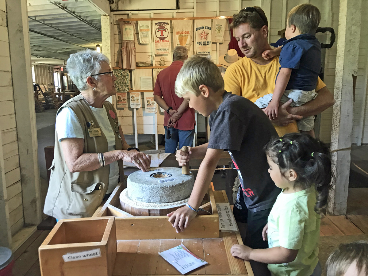 A docent shows a family how to grind grain on a mill stone.