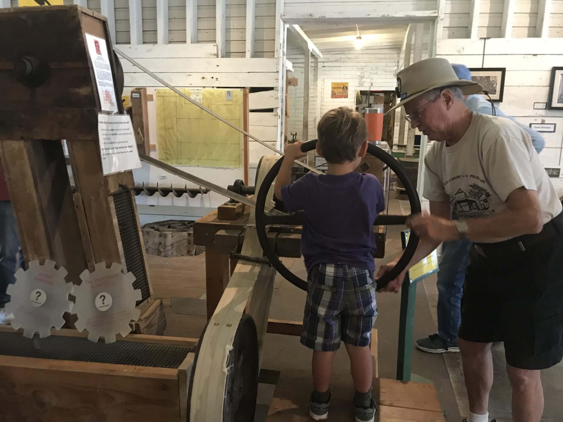 A docent helps my son turn the wheel of an auger.  