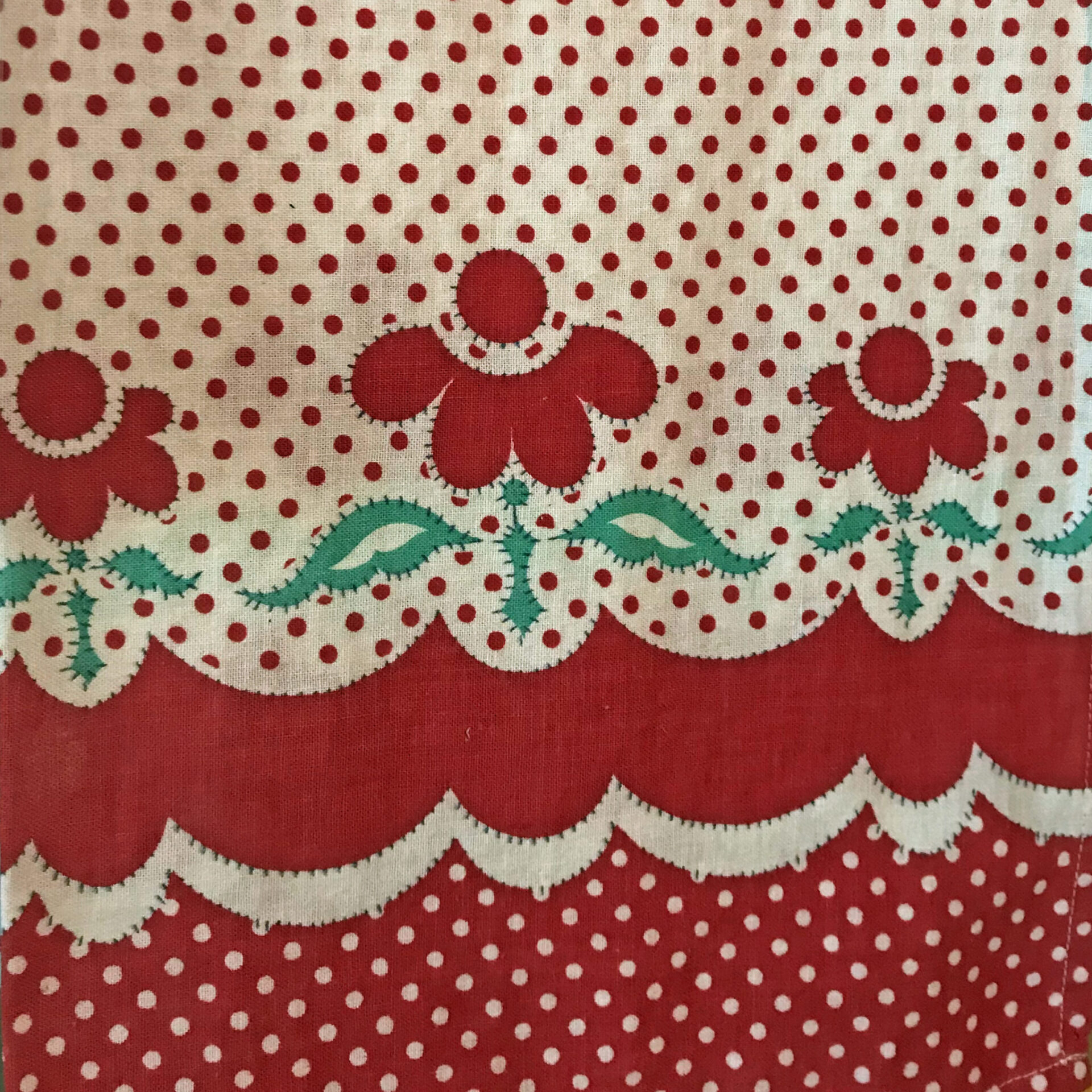 A flour sack with a bright red, white, and green print.  It has polka dots and red flowers.