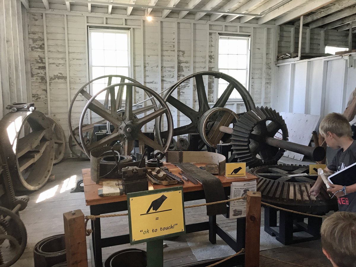 Large metal equipment with gears from the mill's past.  Yellow signs say "okay to touch"