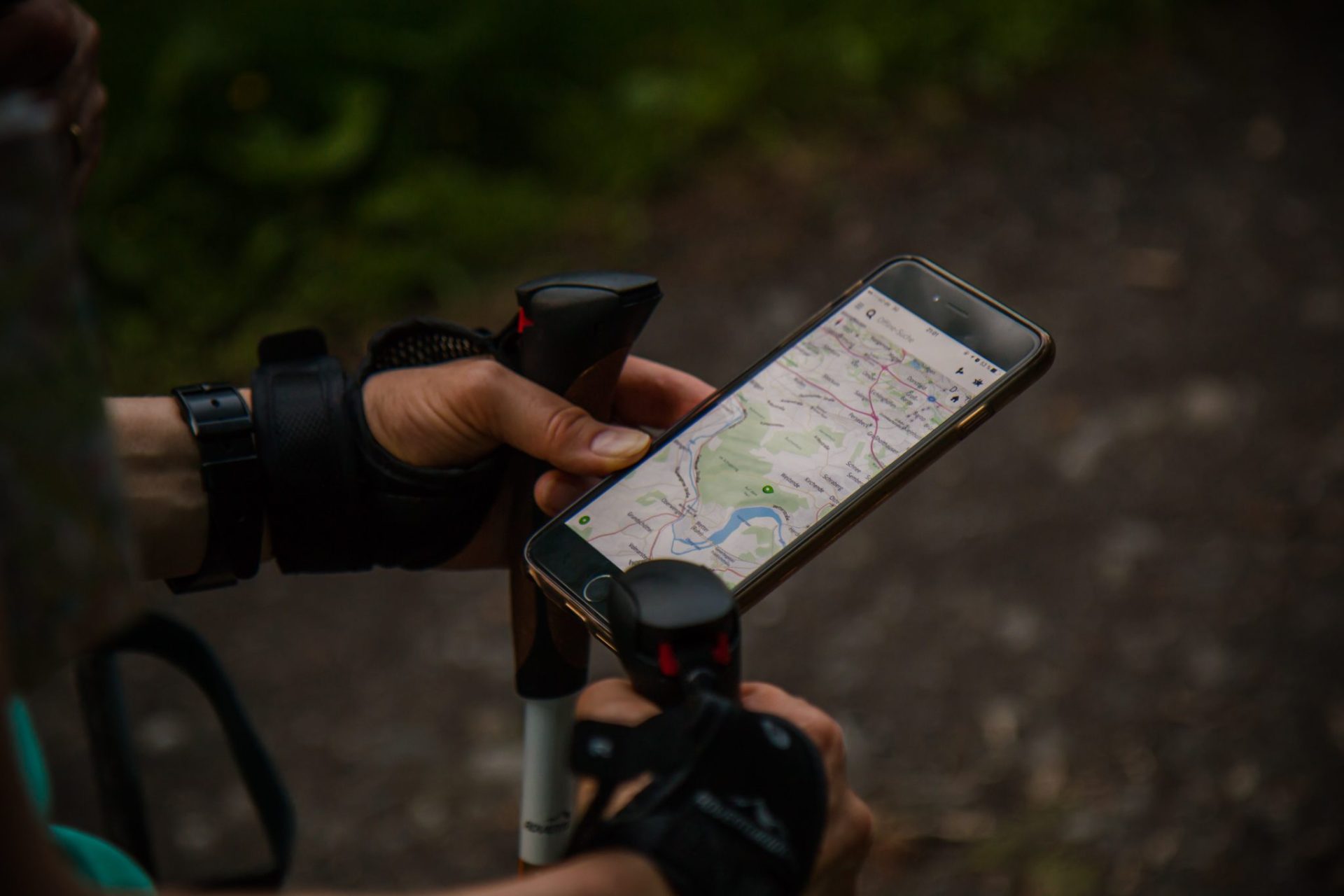 A man with hiking poles holds a phone with a map. 10 essentials for short day hikes